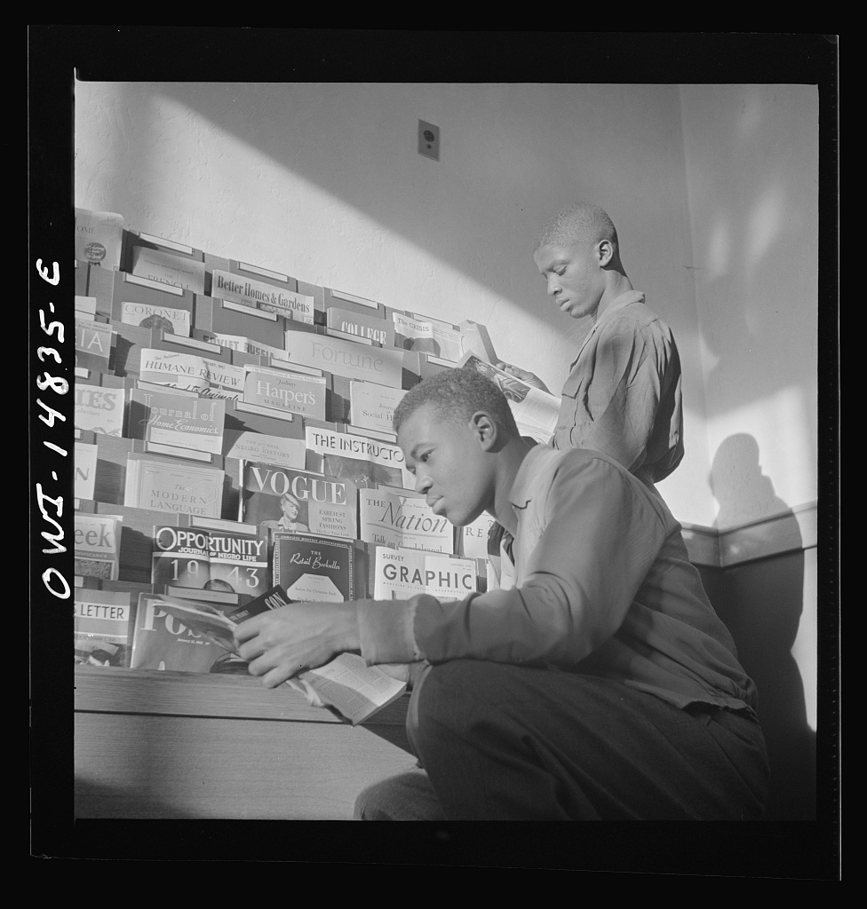 Archival photograph: two students reading periodicals at a library magazine rack.